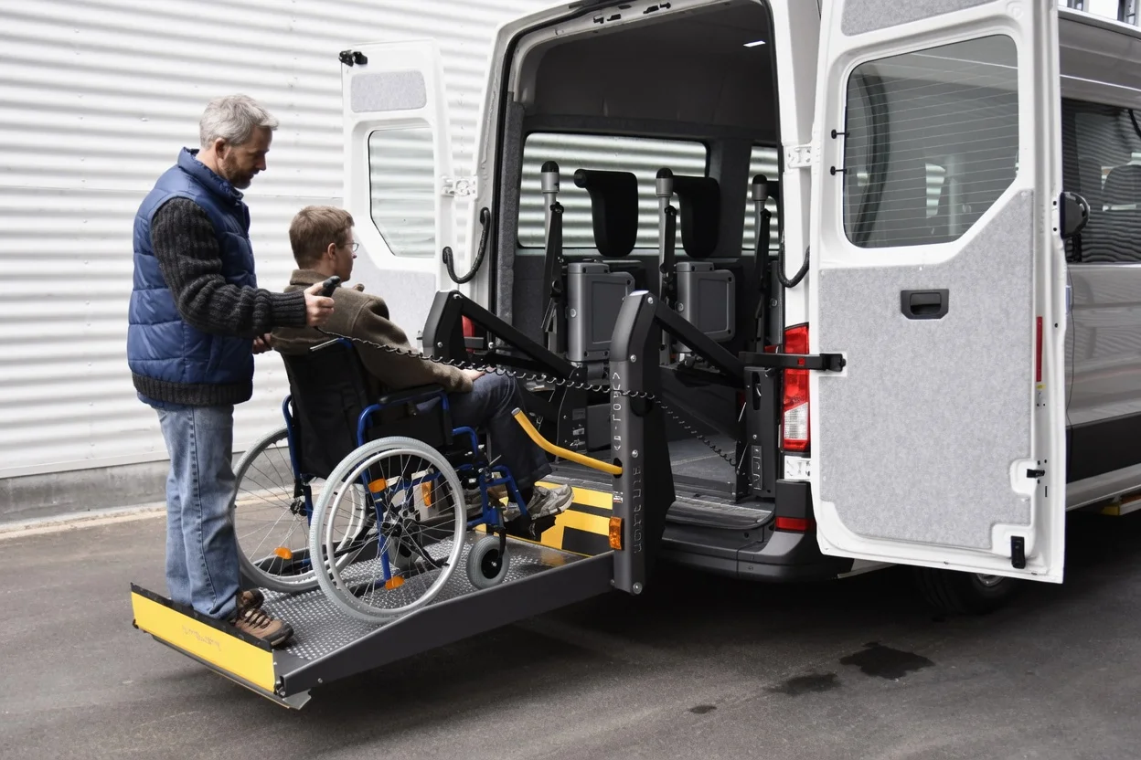 Caregiver assisting a wheelchair user onto the accessible lift of a NYC Wheelchair Transportation van